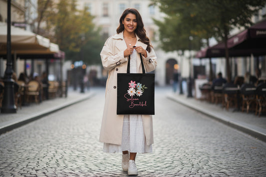 Black tote bag with floral design and 'Salaam Beautiful' text on a wooden surface with sunflower and denim jacket.