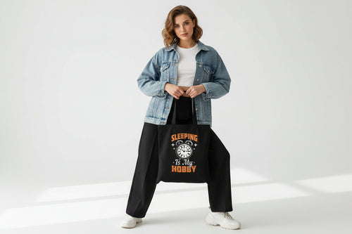 Black tote bag with 'Sleeping is my Hobby' text and clock graphic on a white surface.